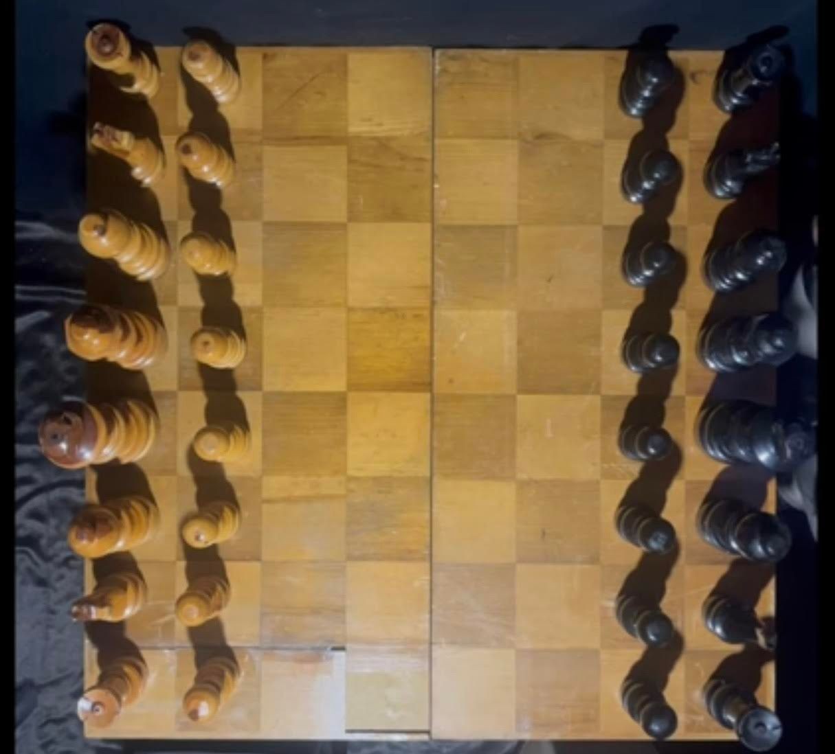 A wooden chessboard with black and white pieces set up for a game, viewed from above.